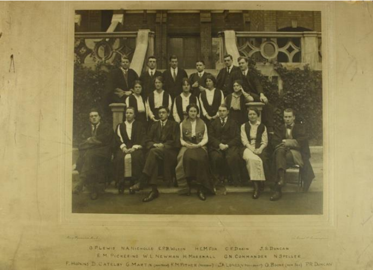 A formal portrait of a group of male and female students sitting outside a University building.