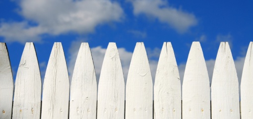 Photograph of a white picket fence against a blue sky
