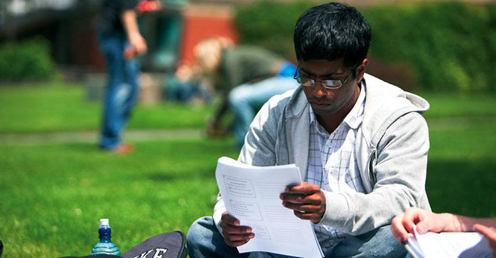 Student studying lecture notes on the grass on campus