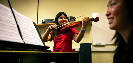 Photograph of two music students in performance practise with violin and piano
