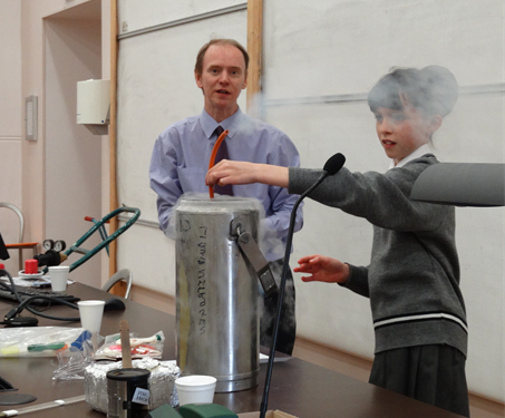 School student conducting experiment with liquid nitrogen supervised by an academic