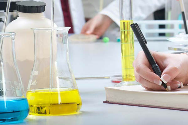Flasks with liquid and woman writing in notepad in lab