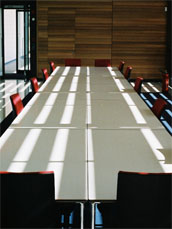 A photo of an empty meeting desk and chairs, with shadows on the table
