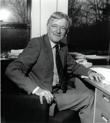 A monochrome image of the late Professor John Stewart, sat working at his desk
