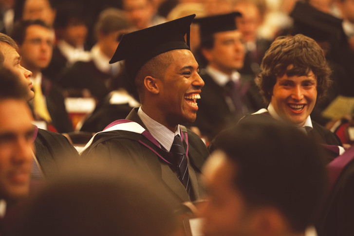 Male student dressed in a gown and mortarboard smiling during his graduation ceremony