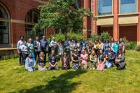 A group shot of 30+ University of Birmingham colleagues outside in the sunshine holding their Green Impact Award plaques