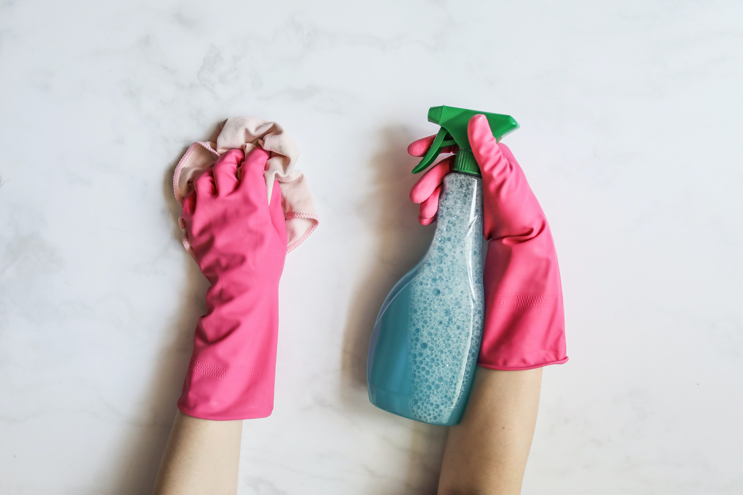 Hands with pink rubber gloves cleaning a marble counter top 