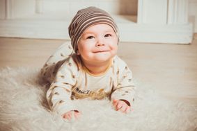 A baby lying on its front, on a fur rug and looking up and smiling