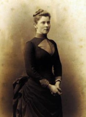 A portrait of Mary Endicott Chamberlain as a young woman, her hair in a bun, wearing a black dress with a frilled bustle.