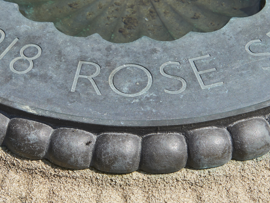 Close up detail of stone birdbath with ornate lead inner bowl featuring close up of inscription of the word 'Rose'
