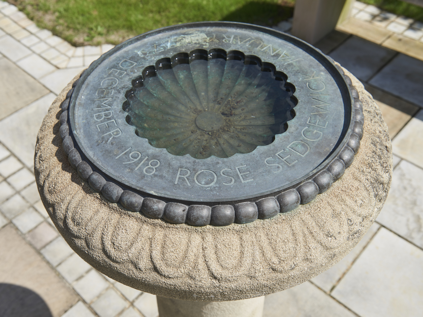 Close up from above of stone birdbath with ornate lead inner bowl, inscribed with the words 'Rose Sedgewick January 1877- December 1918'