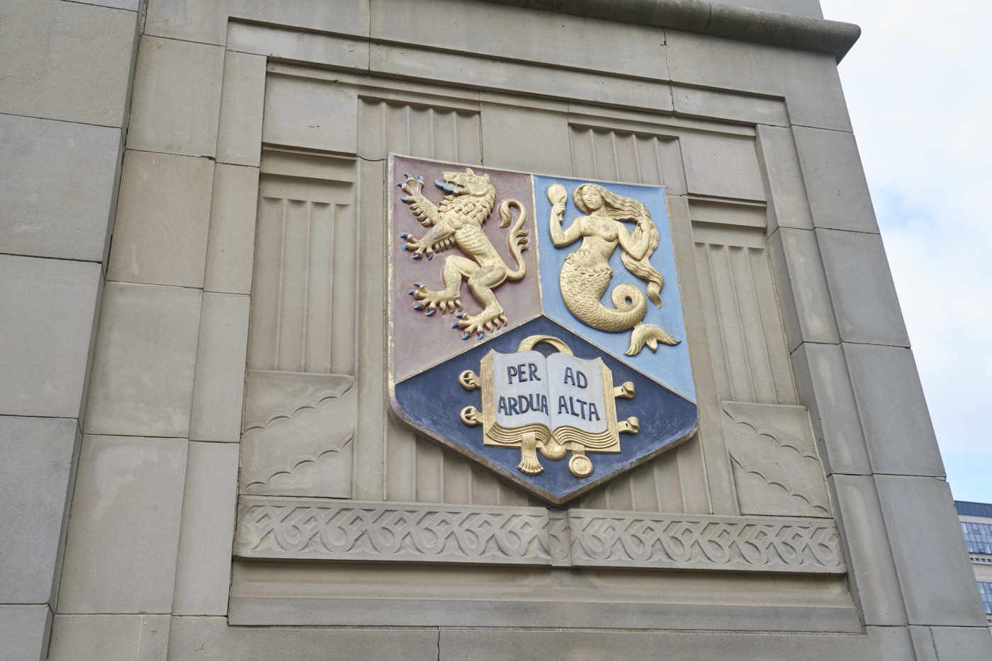 Carved and gilded stone heraldic shield set into the wall of the Barber Institute of Fine Arts by Gordon Herickx featuring a mermaid and a double-headed lion