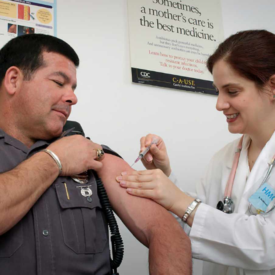 A doctor vaccinating a policeman with a needle in the arm