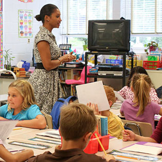 A Teacher walks through a classroom of primary school children as they walk