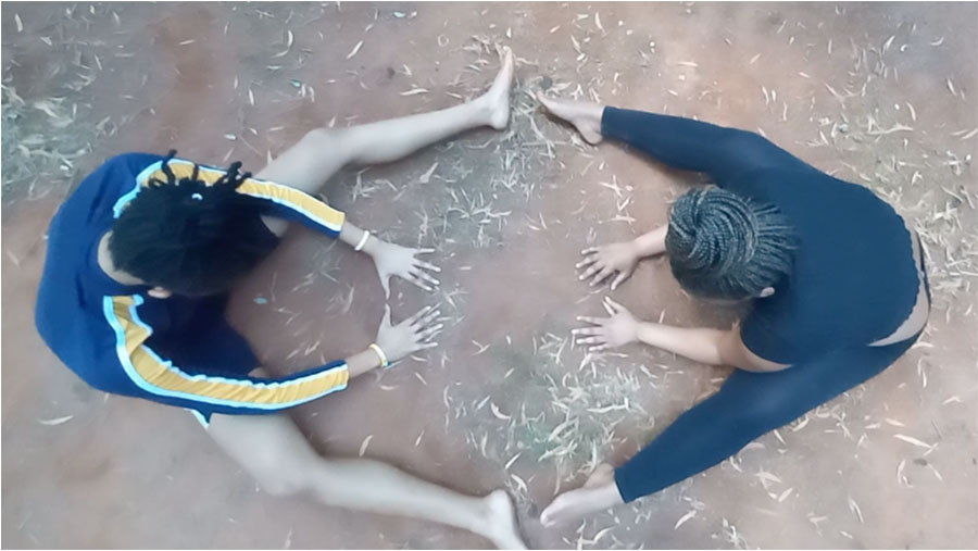 Aerial view looking down on two people sitting on the ground, legs spread, facing each other, but looking at the ground