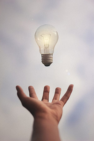 A lit lightbulb hovers above an open hand