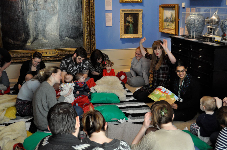 Children and parents sit in the art gallery and listen to an interactive book reading