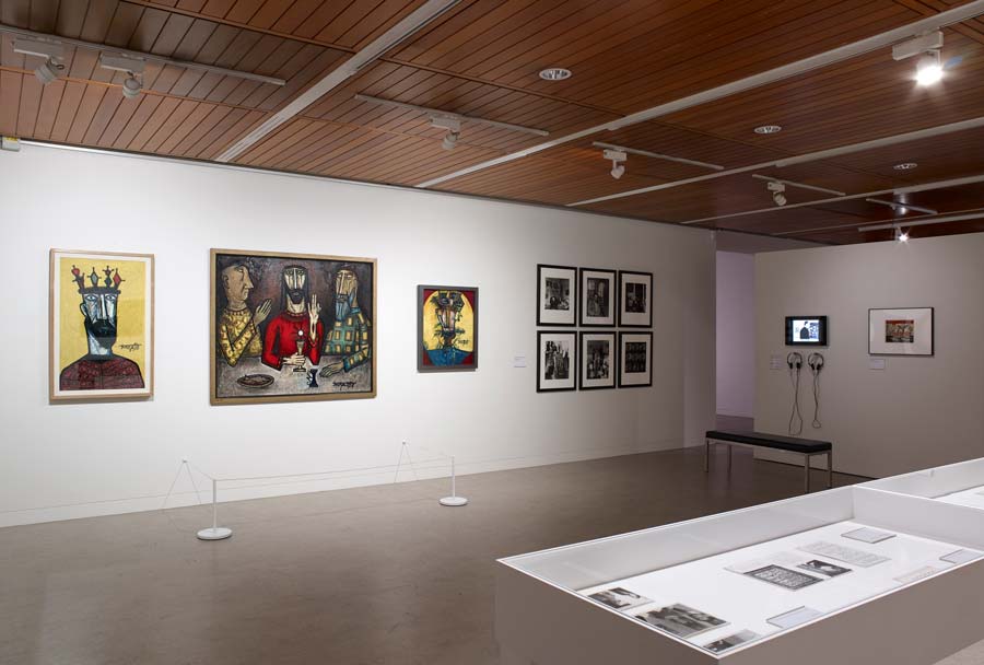 A photograph of an installation of the South Asian Modernists exhibtion at The Whitworth Gallery, showing a number of oil paintings, photographs and a video piece hanging on a wall.