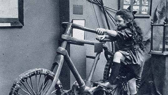 1924 photograph of a young girl attempting to mount a wooden bicycle on display at the British Empire Exhibition