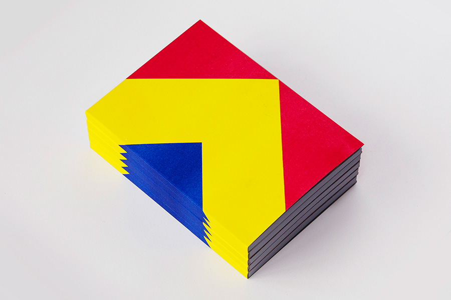 Five ‘Always Forward’ books stacked in a neat pile. The cover is plain, with the striking colours blue, yellow, and red. The blue and yellow form arrows pointing forwards.