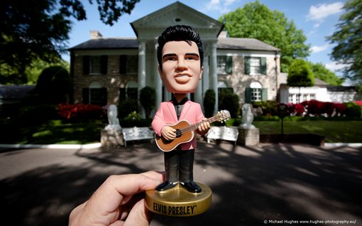 minature elvis figurine being held up in front of graceland 