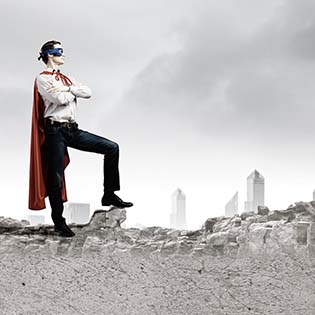 A man in a mask with a cape, posing as a superhero in front of a ruined landscape