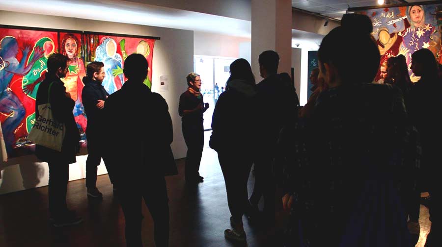 A speaker in a gallery surrounded by a standing audience