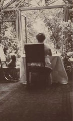 Photograph of Marie Corelli sat in the conservatory with her back to the camera.