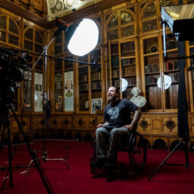 a man in a wheelchair being interviewed with a camera and surrounded by production lights