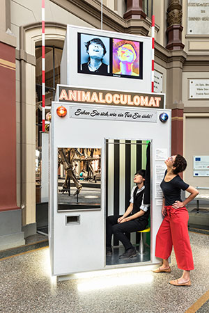 Two participants in an installation in a gallery called animaloculomat based on a photo booth