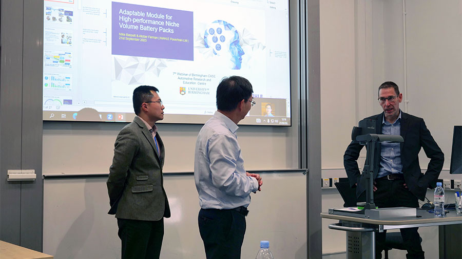 Three male academics standing at the front of a university lecture theatre
