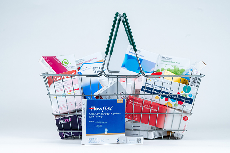 Shopping basket filled with various boxes of tests you can buy in supermarkets and chemists.