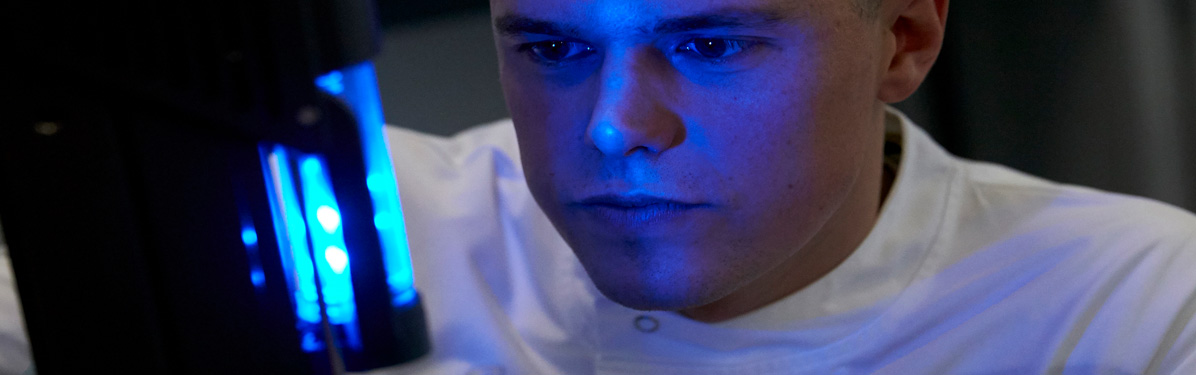 Male lab technician looking at a blue light