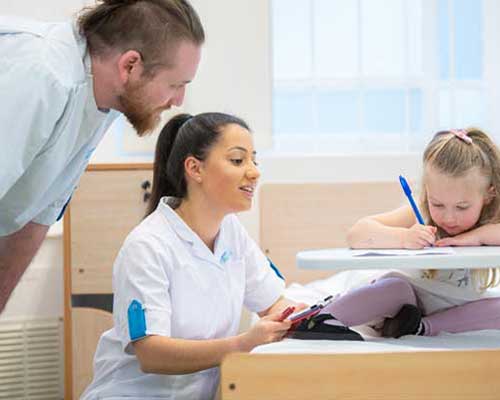 Two nursing students male and female looking at girl writing in an hospital setting