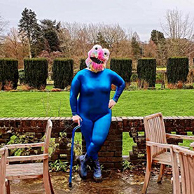 A person in a leotard and muppet mask leaning on a wall