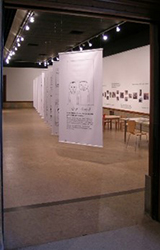 A room that is an art exhibit displaying several tall white banners with art on the banners.