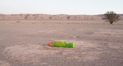 A person wrapped in a bright green body bag on the ground in the desert.