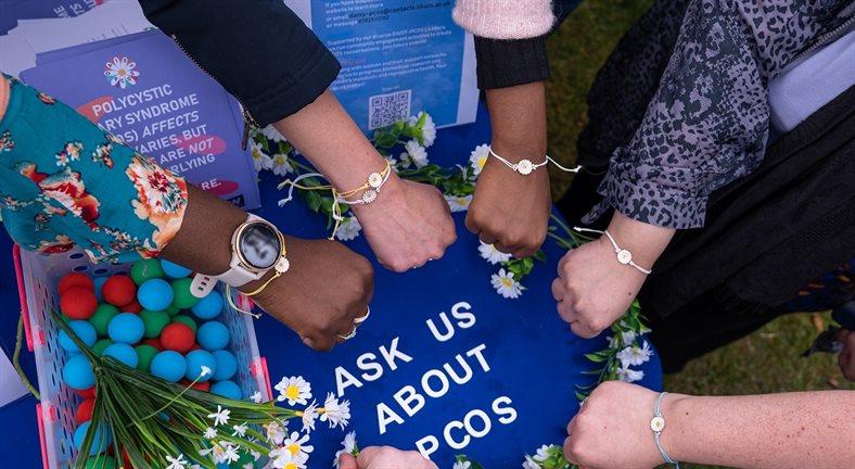 Wrists from several women in the middle with a daisy bracelet around them on the Daisy polycystic ovary syndrome stall