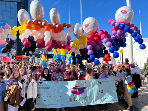 A group of people at Pride 2022 with lots of colourful balloons and banner that says 'Unified at Pride'