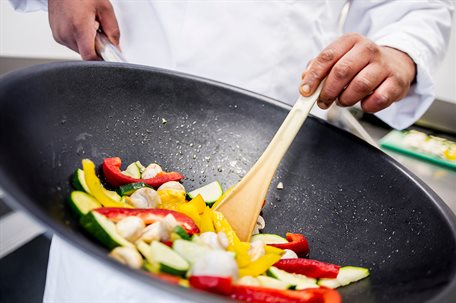 A chef stirring a frying pan containing vegetables