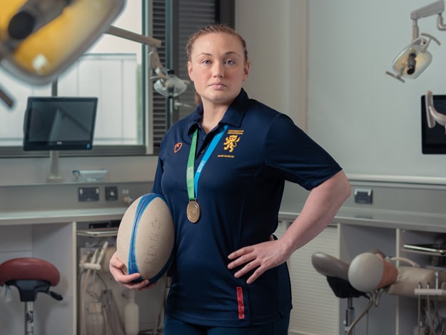 Laura Keates sitting in a dental lab wearing a dental tunic and her Rugby World Cup winners medal.