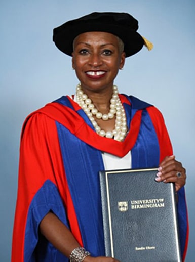 Senior Vice-President of the World Bank, Sandie Okoro, dressed in graduation gown and tam, holding her honorary degree