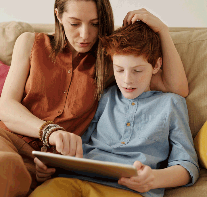 Mother sitting with child as they use smart tablet.