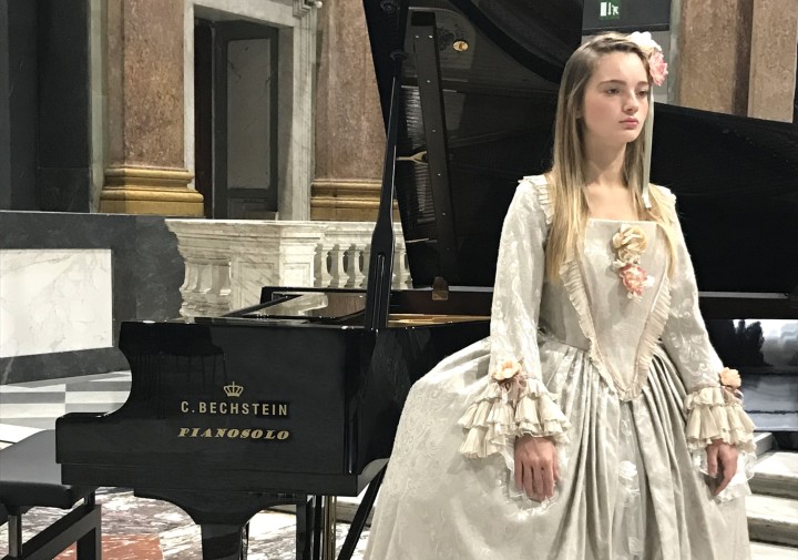 Girl in period costume standing by a grand piano