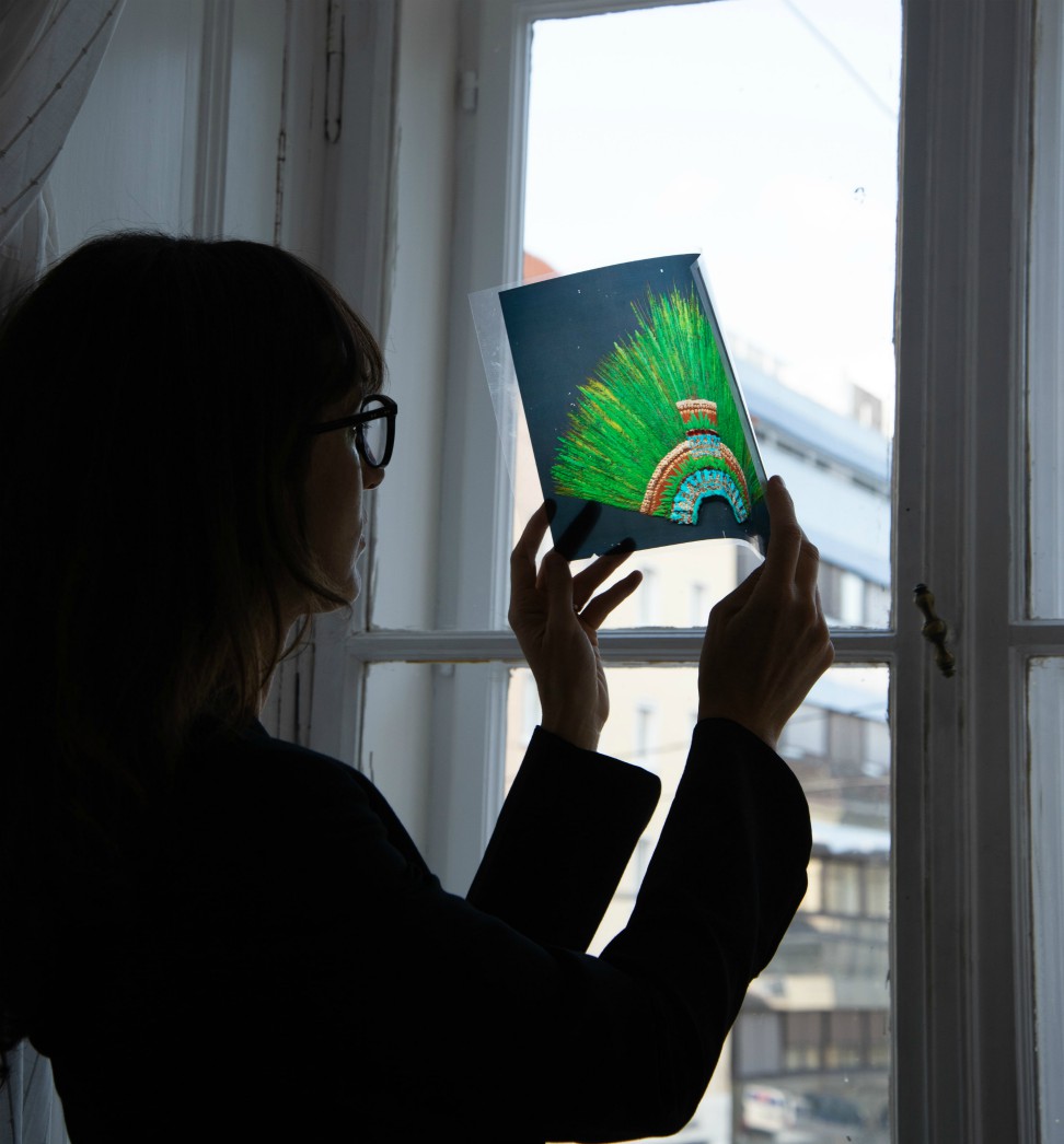 Khadija Von Carroll holds an acetate up to a window with an image of an African headdress on it.