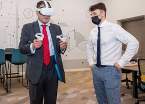 Lord Bilimoria wearing VR headset as MSc Computer Science graduate Andy Morrin looks on