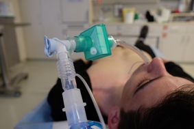 Intubated man lying on a bed in a hospital ward.