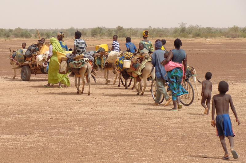 A small group of African migrants travelling across arid terrain on donkeys and carts loaded with their belongings