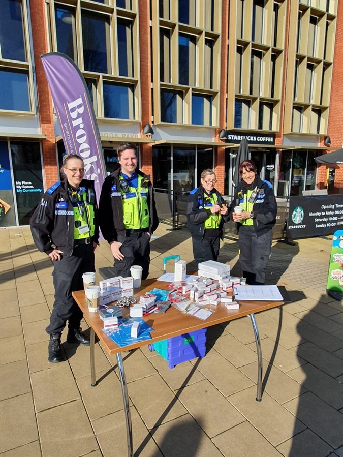 Four officers from the campus police team standing behind a table covered with leaflets and small boxes.