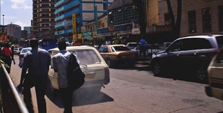Pedestrians on a Nairobi street, walking past a car emitting thick exhaust fumes